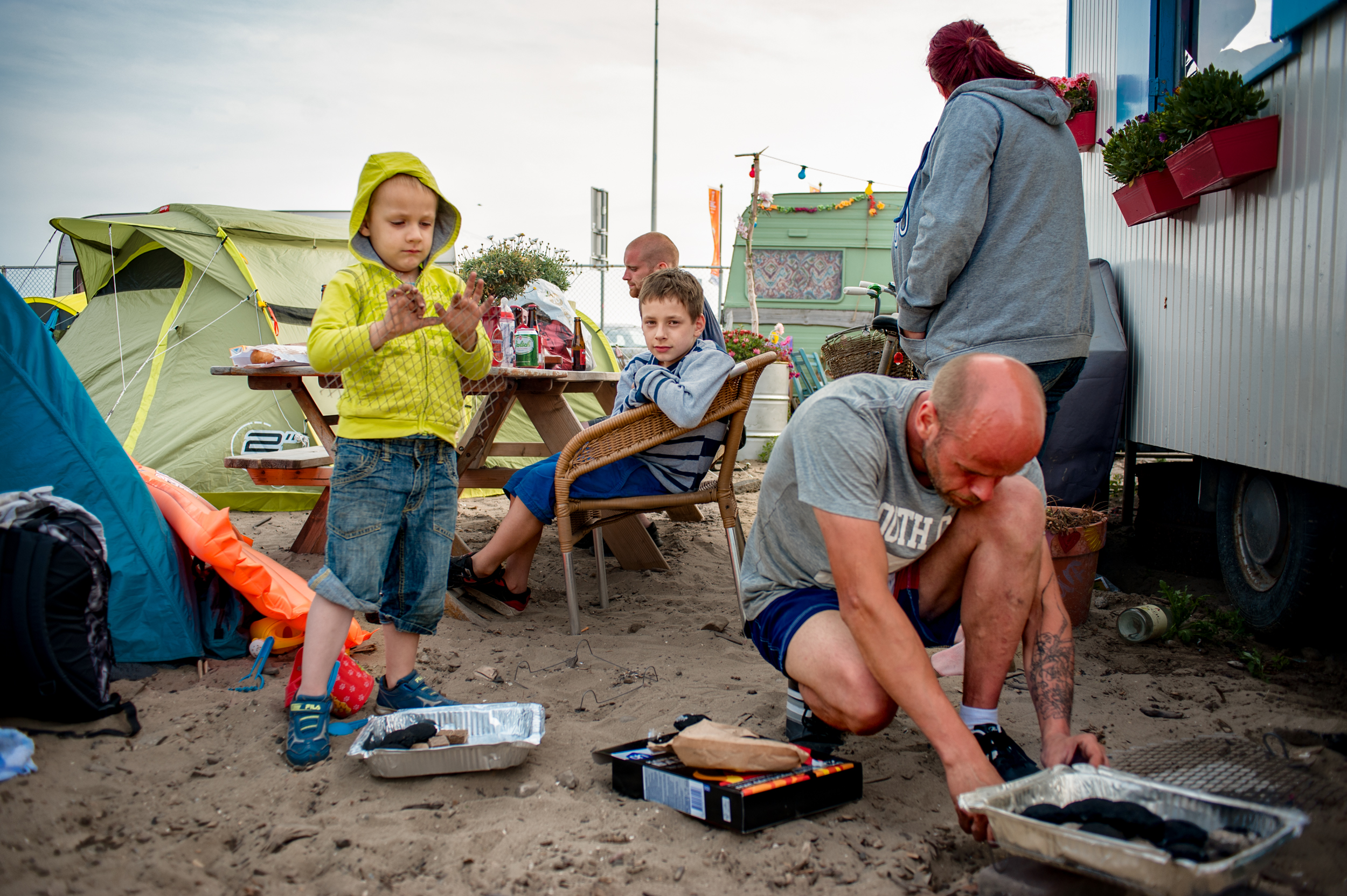 Family in front of their tent; father is lighting the barbecue.