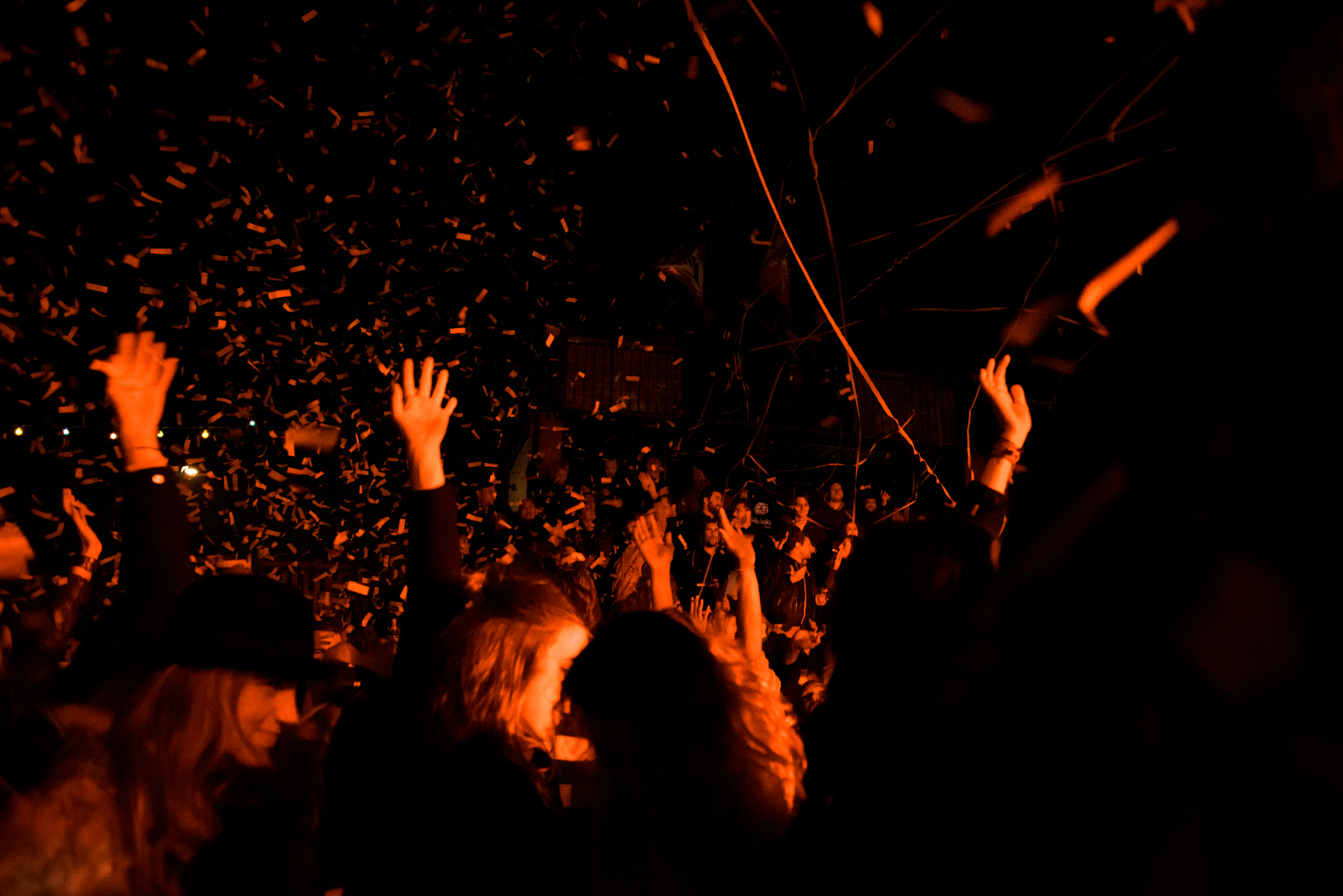 crowd at a night party with hands raised, bonfire glow